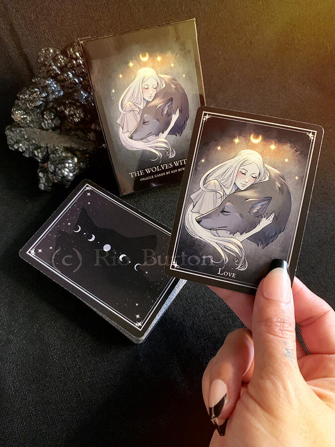 holding up a card from the oracle deck with the deck pictured in the background.